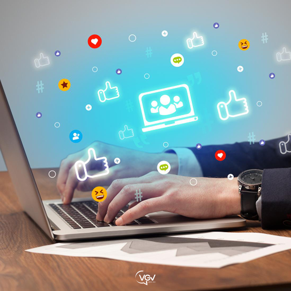 A person works on a laptop with social media icons floating in the air.